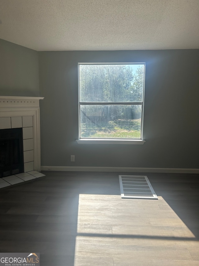 unfurnished living room featuring a textured ceiling, a tile fireplace, and dark wood-type flooring