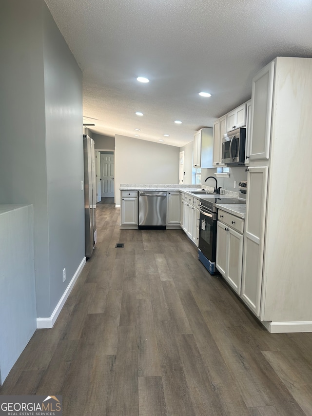 kitchen with vaulted ceiling, stainless steel appliances, dark hardwood / wood-style flooring, and white cabinetry