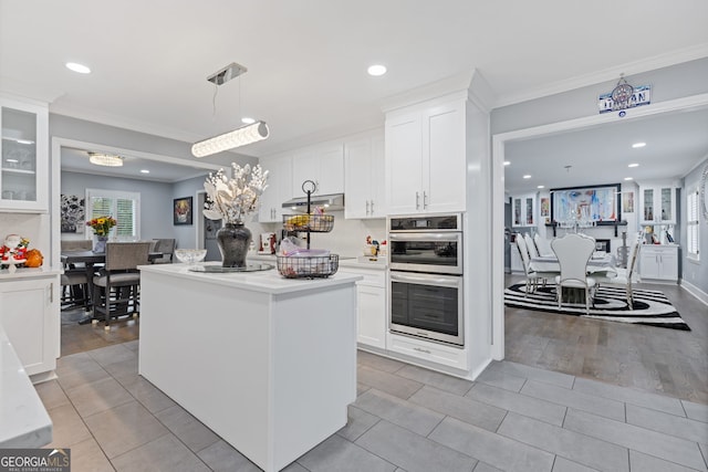 kitchen featuring white cabinetry, stainless steel double oven, light wood-type flooring, decorative light fixtures, and ornamental molding