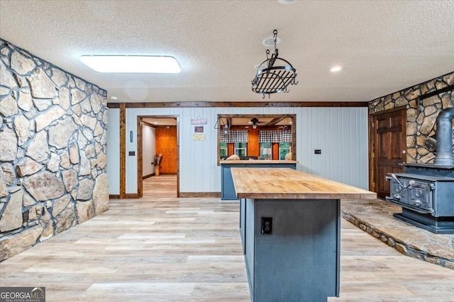 kitchen with wood walls, a wood stove, a textured ceiling, butcher block countertops, and light hardwood / wood-style floors