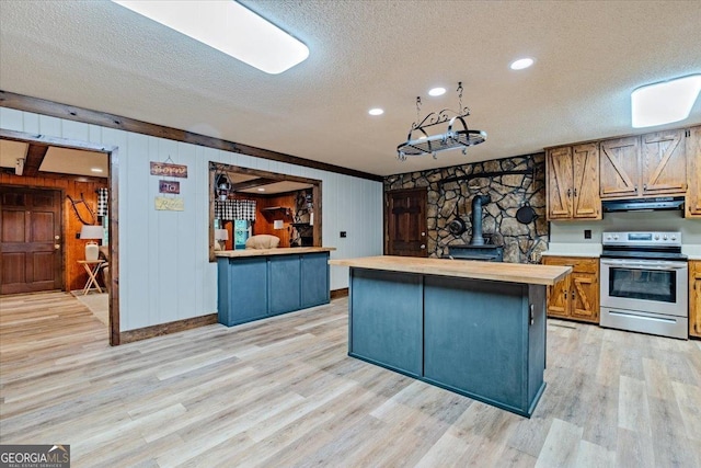 kitchen featuring stainless steel electric range, a wood stove, wooden walls, a textured ceiling, and light hardwood / wood-style floors