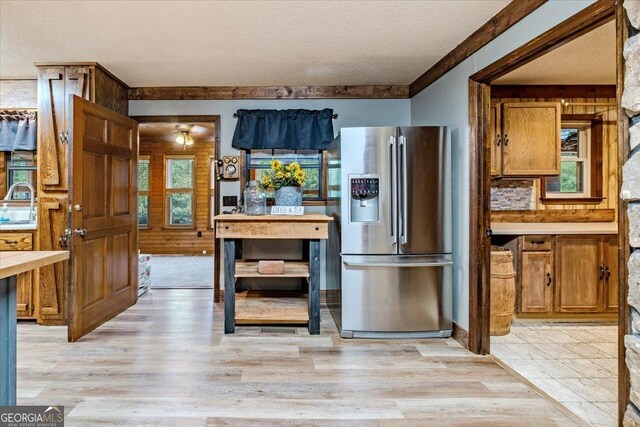 kitchen featuring sink, stainless steel refrigerator with ice dispenser, wooden walls, light hardwood / wood-style flooring, and a textured ceiling