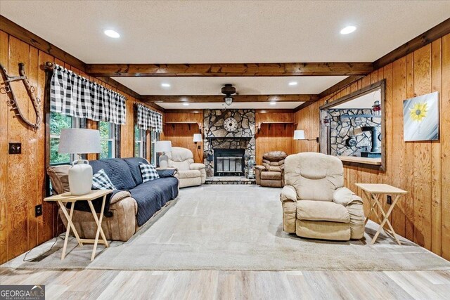 living room featuring beam ceiling, a stone fireplace, wooden walls, and light hardwood / wood-style flooring