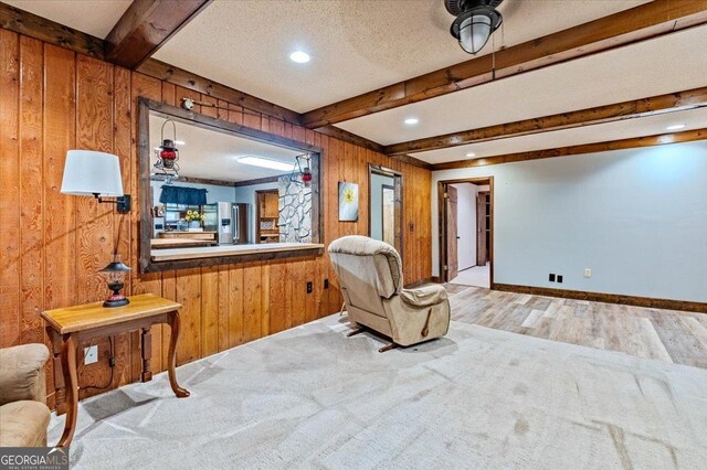 sitting room with wood walls, beam ceiling, and light carpet