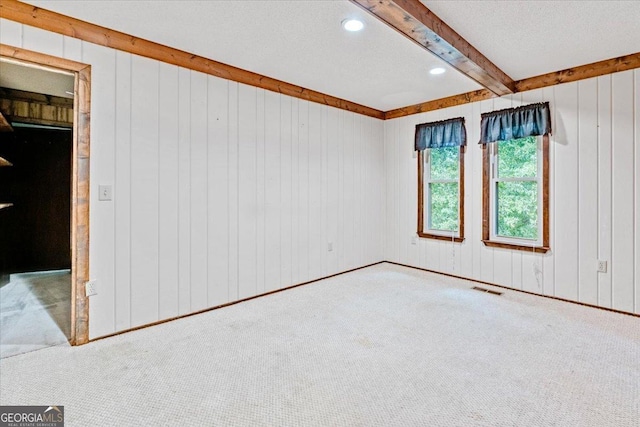 unfurnished room featuring beam ceiling, carpet floors, a textured ceiling, and wooden walls