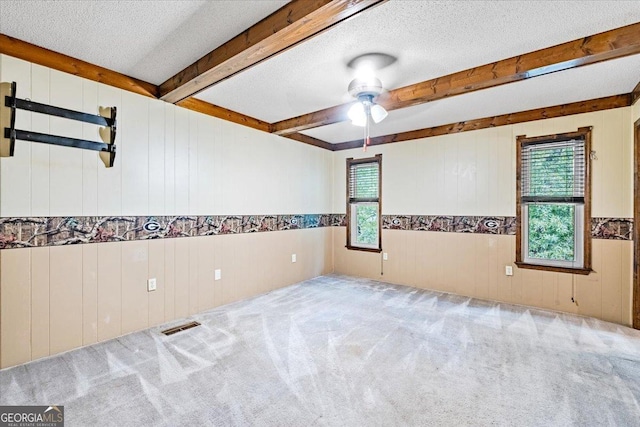 spare room with beam ceiling, light colored carpet, a wealth of natural light, and ceiling fan