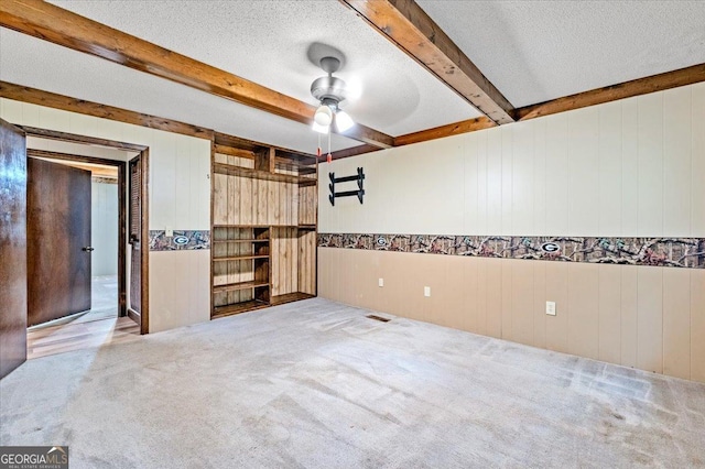 carpeted empty room with beamed ceiling, ceiling fan, wood walls, and a textured ceiling