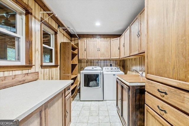 clothes washing area with washing machine and dryer, wooden walls, cabinets, and a textured ceiling