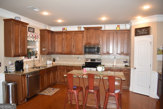 kitchen with appliances with stainless steel finishes, a kitchen island, dark hardwood / wood-style flooring, ornamental molding, and sink