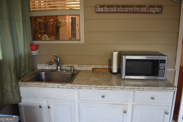 kitchen featuring wooden walls, white cabinetry, and sink