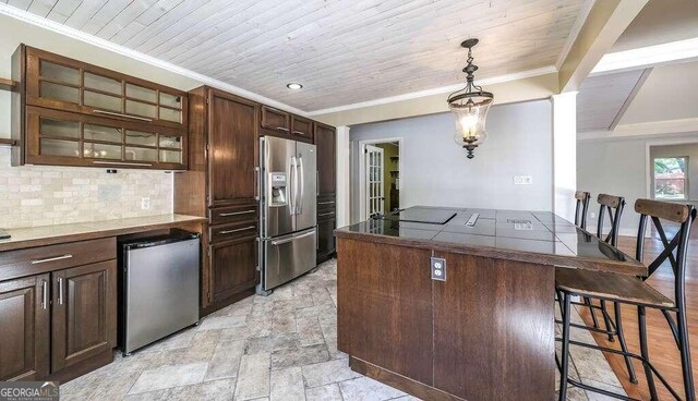 kitchen featuring dark brown cabinetry, decorative light fixtures, stainless steel fridge, and a breakfast bar