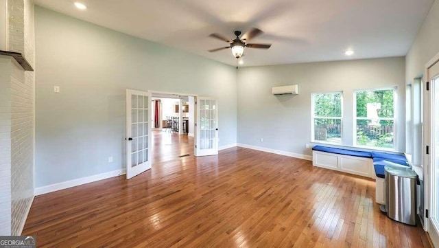 unfurnished living room with light wood-type flooring, lofted ceiling, ceiling fan, french doors, and a wall mounted AC