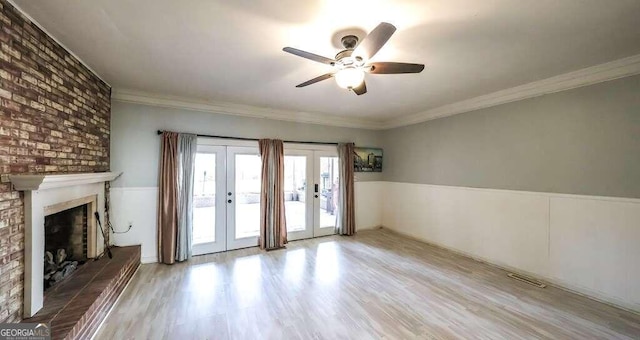 unfurnished living room with ceiling fan, light wood-type flooring, french doors, a fireplace, and crown molding