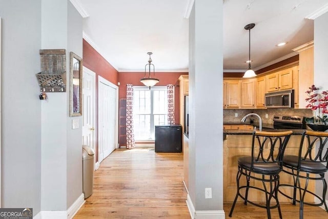 kitchen with light hardwood / wood-style floors, appliances with stainless steel finishes, decorative light fixtures, ornamental molding, and light brown cabinetry