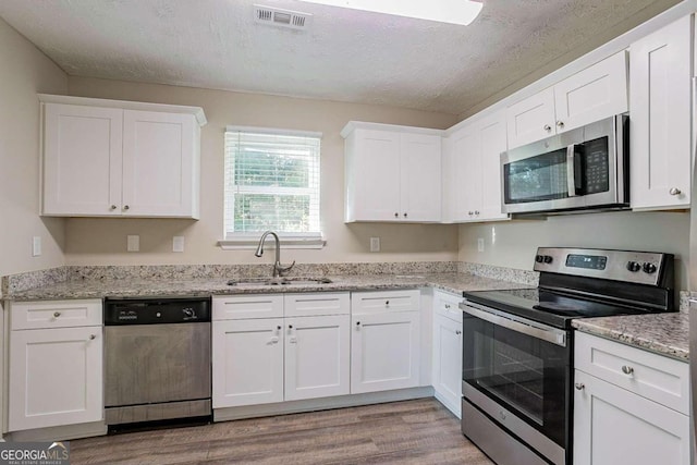 kitchen featuring white cabinets, stainless steel appliances, sink, and light hardwood / wood-style flooring