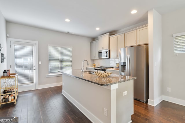 kitchen with an island with sink, sink, appliances with stainless steel finishes, dark hardwood / wood-style floors, and dark stone counters