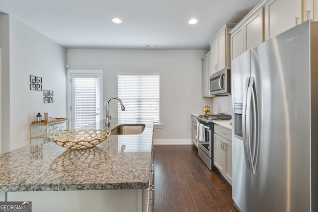 kitchen with light stone counters, sink, a center island with sink, appliances with stainless steel finishes, and dark hardwood / wood-style flooring