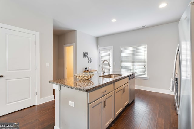 kitchen featuring sink, a kitchen island with sink, stone counters, stainless steel appliances, and dark hardwood / wood-style floors