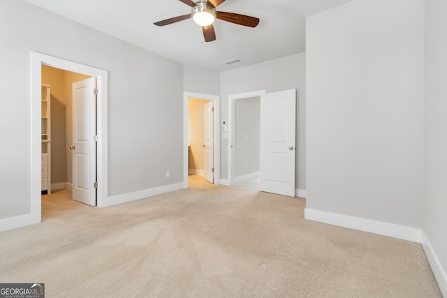 unfurnished bedroom featuring connected bathroom, a spacious closet, ceiling fan, and light colored carpet