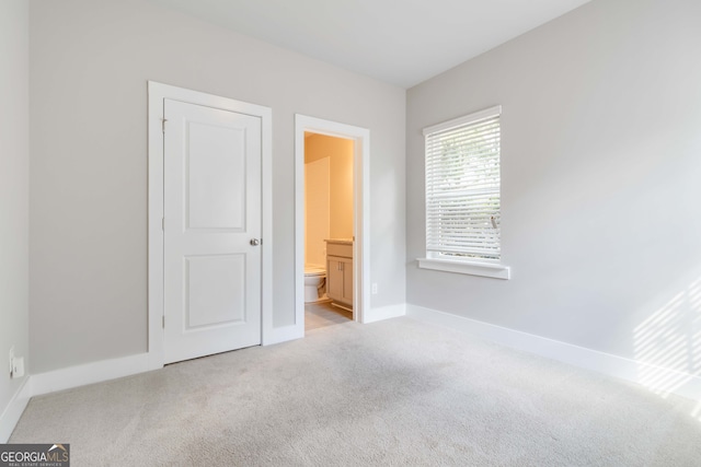 unfurnished bedroom featuring light carpet and connected bathroom