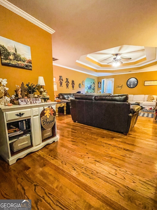 living room with ceiling fan, a tray ceiling, hardwood / wood-style floors, and ornamental molding