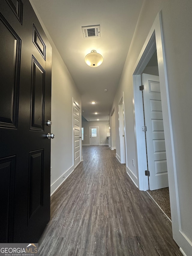 hallway featuring dark wood-type flooring, baseboards, and visible vents