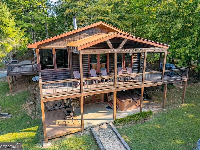 back of house with a hot tub, log veneer siding, a patio, a deck, and a yard