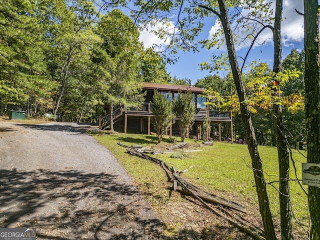 view of front facade with gravel driveway, stairs, a deck, and a front yard