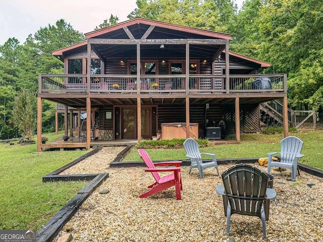 rear view of house featuring a lawn, a hot tub, a deck, faux log siding, and a fire pit