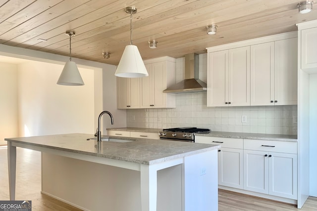 kitchen with a kitchen island with sink, hanging light fixtures, wall chimney exhaust hood, and sink