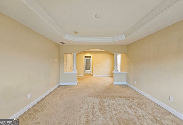 empty room with ornamental molding, a tray ceiling, light colored carpet, and ornate columns