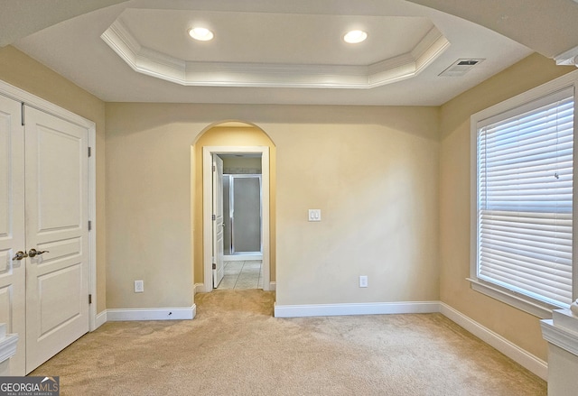 unfurnished bedroom with a raised ceiling, crown molding, light carpet, and a closet