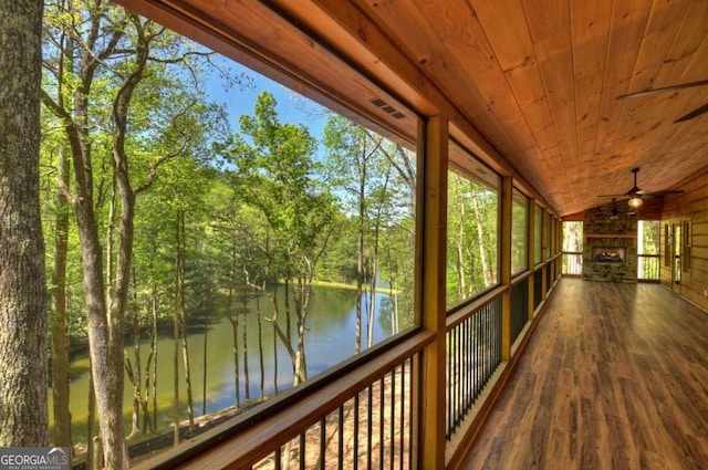 unfurnished sunroom featuring ceiling fan, lofted ceiling, wooden ceiling, a water view, and an outdoor stone fireplace