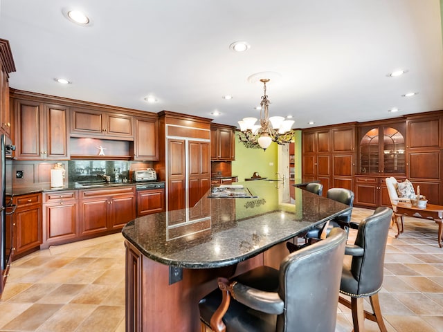 kitchen featuring dark stone countertops, a kitchen island, a breakfast bar area, decorative light fixtures, and a notable chandelier