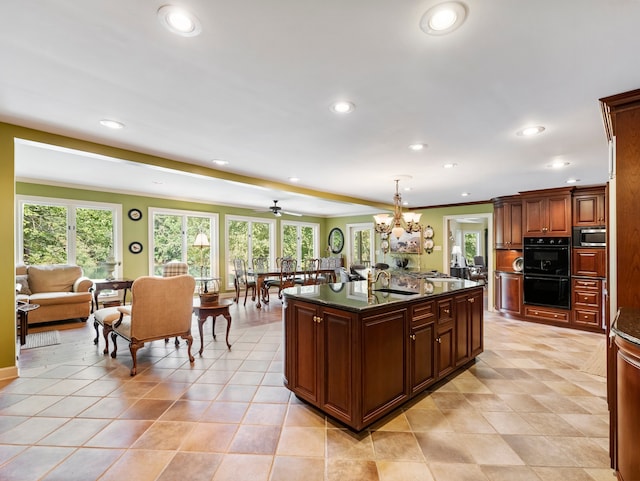 kitchen featuring pendant lighting, a kitchen island with sink, ceiling fan with notable chandelier, stainless steel microwave, and double oven