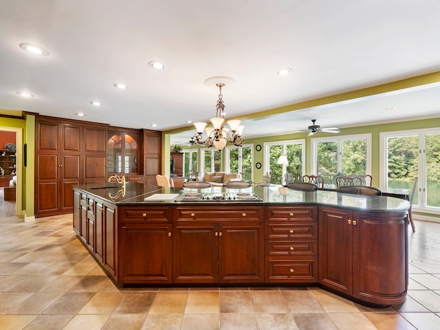 kitchen with a large island, dark stone counters, ceiling fan with notable chandelier, decorative light fixtures, and stainless steel cooktop