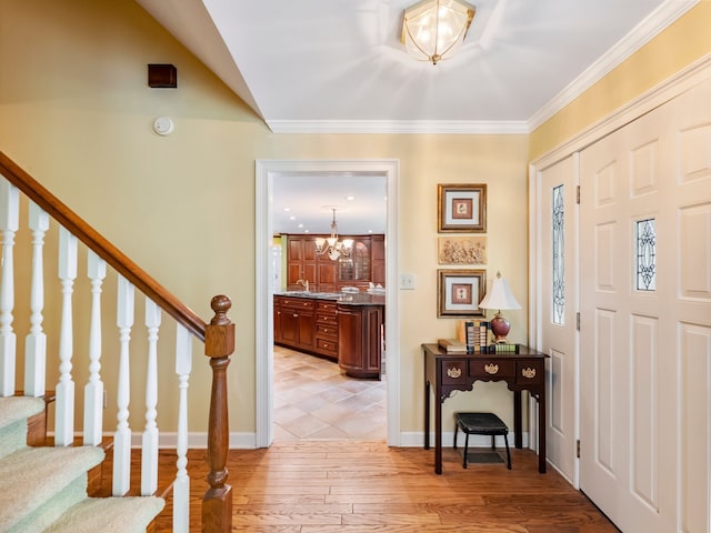 foyer entrance with sink, light wood-type flooring, crown molding, and a chandelier