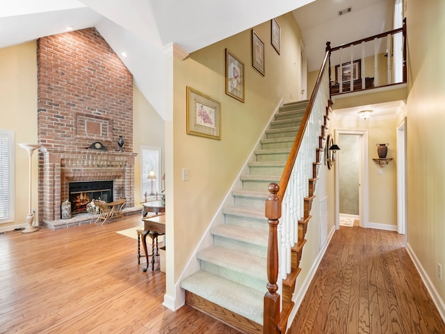 stairs featuring high vaulted ceiling, a brick fireplace, and hardwood / wood-style flooring