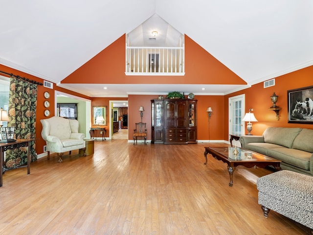 living room with light hardwood / wood-style flooring, crown molding, and high vaulted ceiling