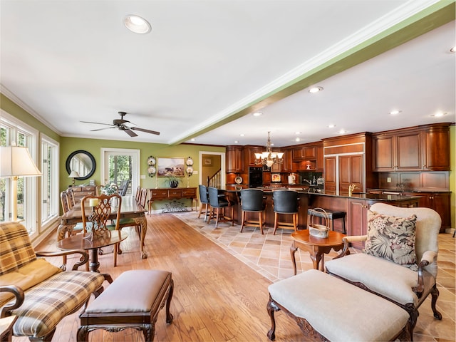 living room with ceiling fan with notable chandelier, crown molding, and light hardwood / wood-style flooring