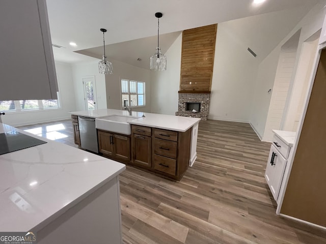 kitchen featuring pendant lighting, a fireplace, an island with sink, sink, and stainless steel dishwasher