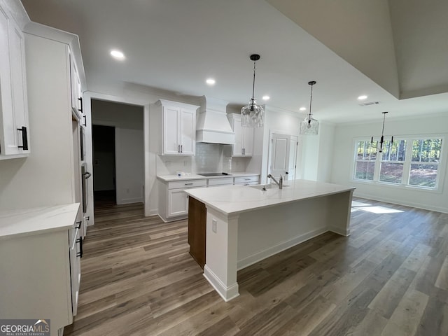 kitchen with sink, premium range hood, white cabinetry, an island with sink, and a barn door