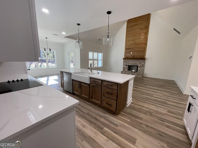 kitchen with pendant lighting, an island with sink, sink, hardwood / wood-style flooring, and a brick fireplace