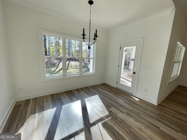 unfurnished dining area featuring dark wood-type flooring, ornamental molding, and a chandelier