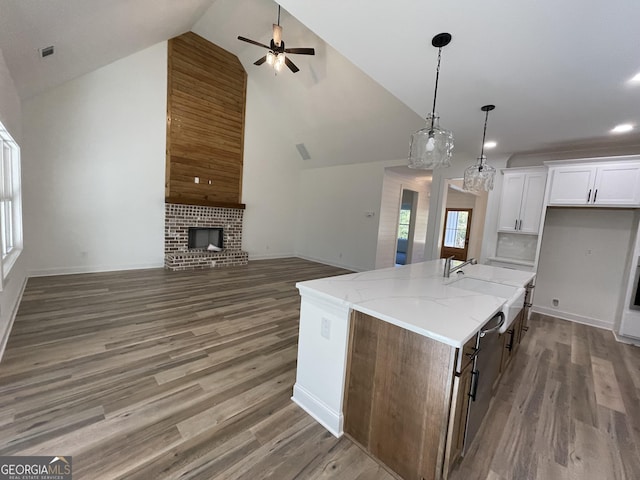 kitchen with a fireplace, white cabinets, dark hardwood / wood-style flooring, light stone counters, and a center island with sink