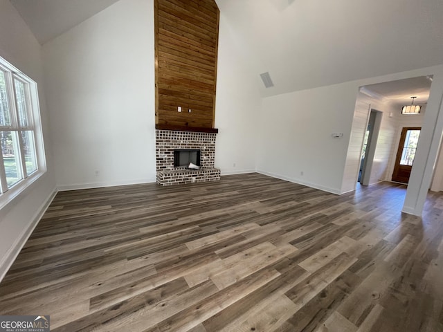 unfurnished living room with dark hardwood / wood-style flooring, a brick fireplace, and high vaulted ceiling