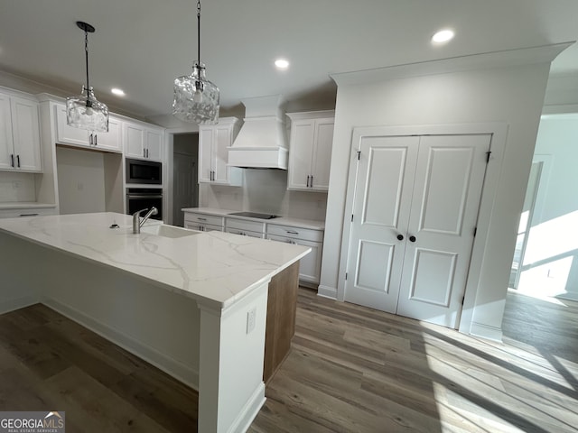 kitchen featuring white cabinetry, pendant lighting, custom range hood, and a center island with sink