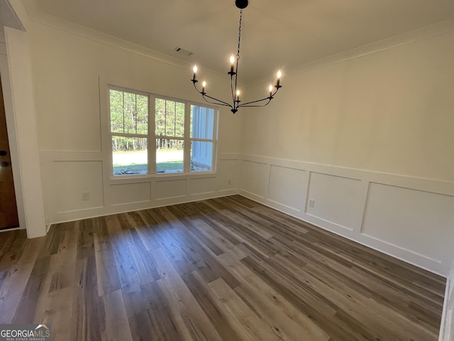 unfurnished dining area featuring dark wood-type flooring, ornamental molding, and a chandelier