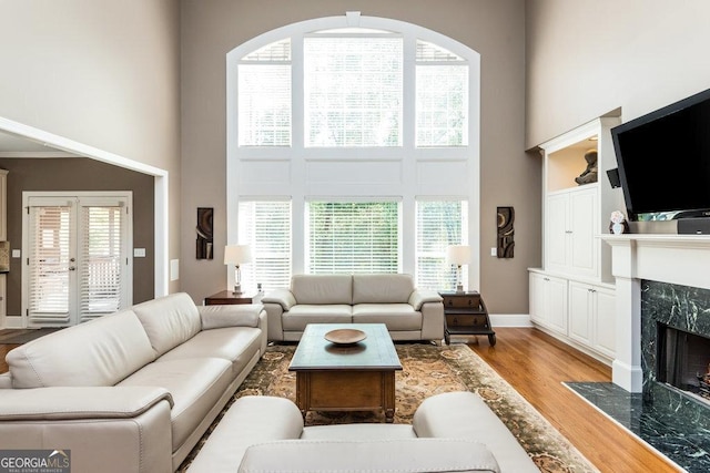 living room with a high end fireplace, a high ceiling, and light hardwood / wood-style flooring