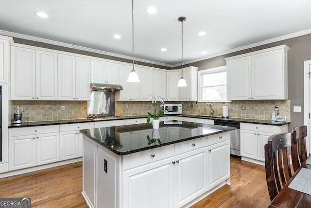 kitchen featuring appliances with stainless steel finishes, decorative light fixtures, light hardwood / wood-style flooring, white cabinets, and a center island